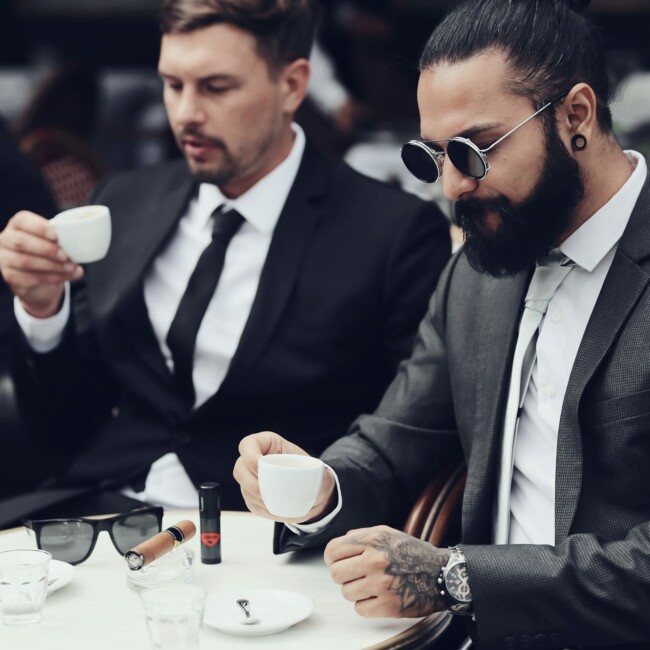 zwei Männer im Anzug sitzen am Tisch und trinken Espresso