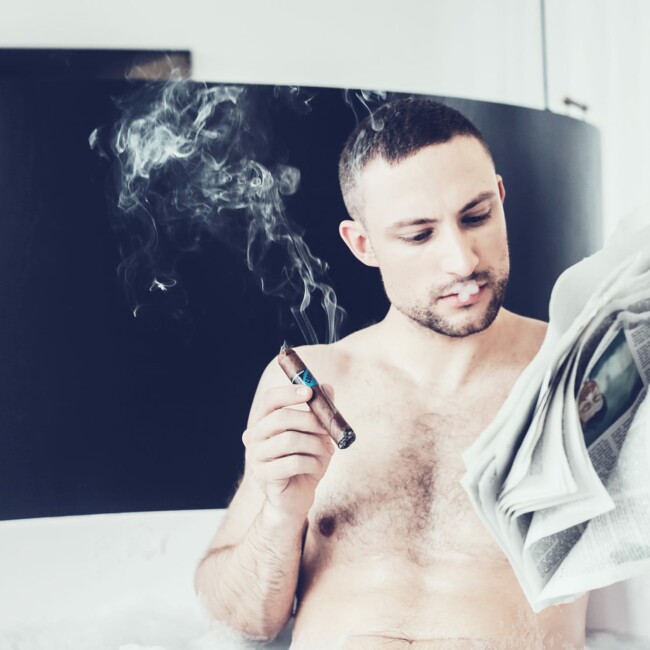 Mann liegt in der Badewanne und liest Zeitung, dabei rauchte r eine Zigarre