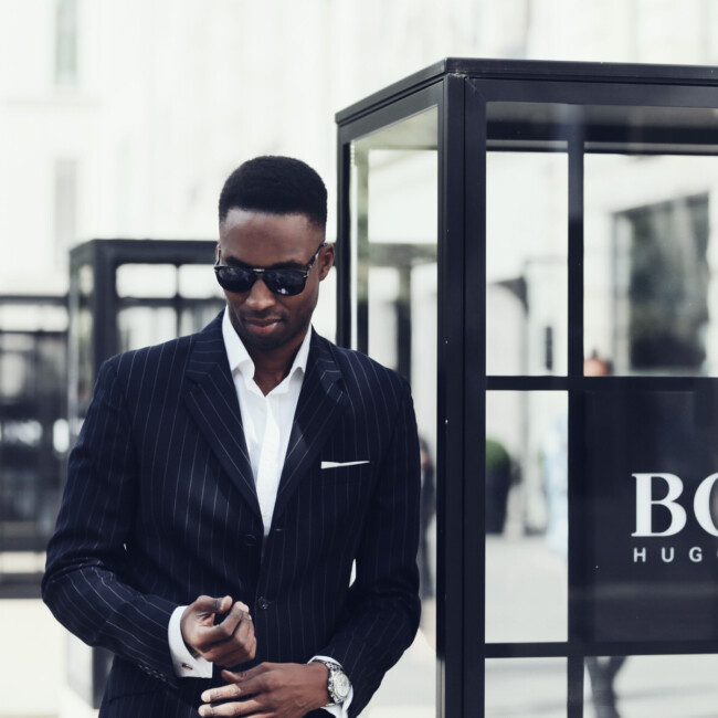 Mann im schwarzen Anzug und Sonnenbrille steht vor einer Hugo Boss Außenwerbung