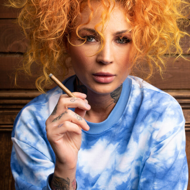 Frau mit orangen Haaren hält eine Zigarette in der Hand