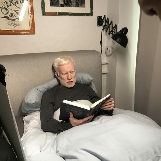 Mann mit blauen kabellosen Bluetooth Kopfhörern liegt im Bett und ließt ein Buch